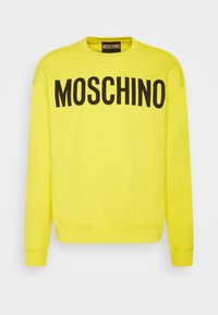 Jasnożółta bluza z długim rękawem z czarnym logo „MOSCHINO” na wysokości klatki piersiowej oraz pasującą metką wewnątrz kołnierzyka.