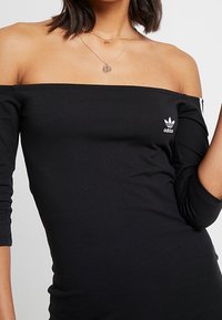 Svart avskuren topp med lättviktsmaterial, med trekvartslånga ärmar och en liten vit Adidas-logotyp på bröstet.