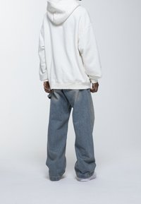 Felpa bianca oversize con un tessuto testurizzato, abbinata a jeans baggy blu chiaro. I jeans presentano una leggera sfumatura e sono risvoltati alla caviglia.