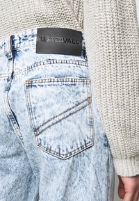 Vaqueros de mezclilla azul claro desgastados con un parche de logotipo JUSTCAVALLI en cuero negro en la cintura. Cuenta con un bolsillo trasero con detalles de costura.