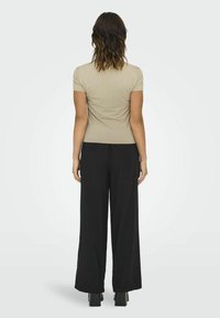 Beige kortærmet top kombineret med sorte bukser med vidde. Outfittet har en tætsiddende design og en glat stoftekstur.