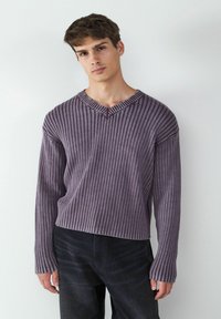 Lila gerippter Strickpullover mit V-Ausschnitt und überschnittenen Schultern. Verfügt über lange Ärmel und einen leicht verkürzten Saum. Der Stoff wirkt weich und strukturiert.