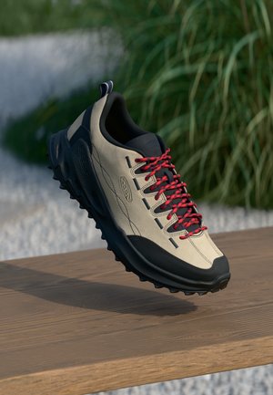 Beige buiten schoen met zwarte accenten en rode veters. Beschikt over een gestructureerde zool voor grip, glad bovenmateriaal en een logo-detail bij de hak.