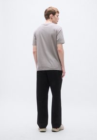 Γκρι βαμβακερό μπλουζάκι με στρογγυλή λαιμόκοψη, κοντά μανίκια και χαλαρή εφαρμογή, συνδυασμένο με μαύρο παντελόνι με φαρδιά μπατζάκια και ανοιχτόχρωμα αθλητικά παπούτσια.