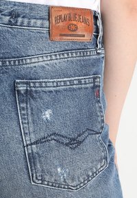 Kapsa z modrých džínů z denimu s opotřebovanou strukturou, bílým švem a hnědou koženou nášivkou s označením "REPLAY BLUE JEANS".