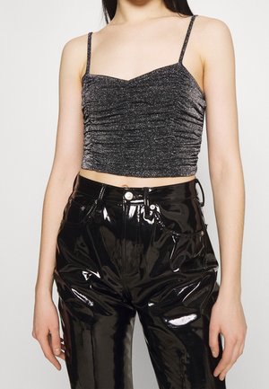 Černý třpytivý crop top s nastavitelnými tenkými ramínky, s nařaseným designem a hladkou, lesklou texturou. V kombinaci s lesklými černými kalhotami.
