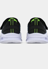 Pár černých tenisek s neonově zelenými akcenty a bílými texturovanými podešvami zobrazený z pohledu zezadu na čistém bílém pozadí.