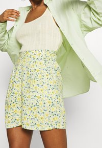 Květinová sukně se žlutými a zelenými vzory, s nařaseným pasem, spojená s světle zelenou oversized košilí a krémovým žebrovaným tílkem.