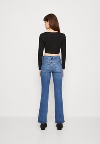 Top corto nero a maniche lunghe abbinato a jeans azzurri a vita alta e svasati. Tessuto morbido, silhouette aderente e design minimalista.