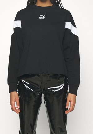 Sweatshirt noir avec accents blancs aux épaules et logo Puma, présentant une couture en V, des manches longues et une coupe cropped. Assorti à un pantalon noir brillant.