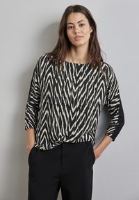 Czarny i kremowy top w wzory z dekoltem łódkowym i rękawami dosięgającymi łokcia; charakteryzuje się kontrastującym czarnym detalem z boku oraz luźnym krojem.