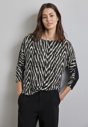 Top a motivi black e crema con scollatura a barca e maniche a tre quarti; presenta un dettaglio laterale nero in contrasto e una vestibilità rilassata.