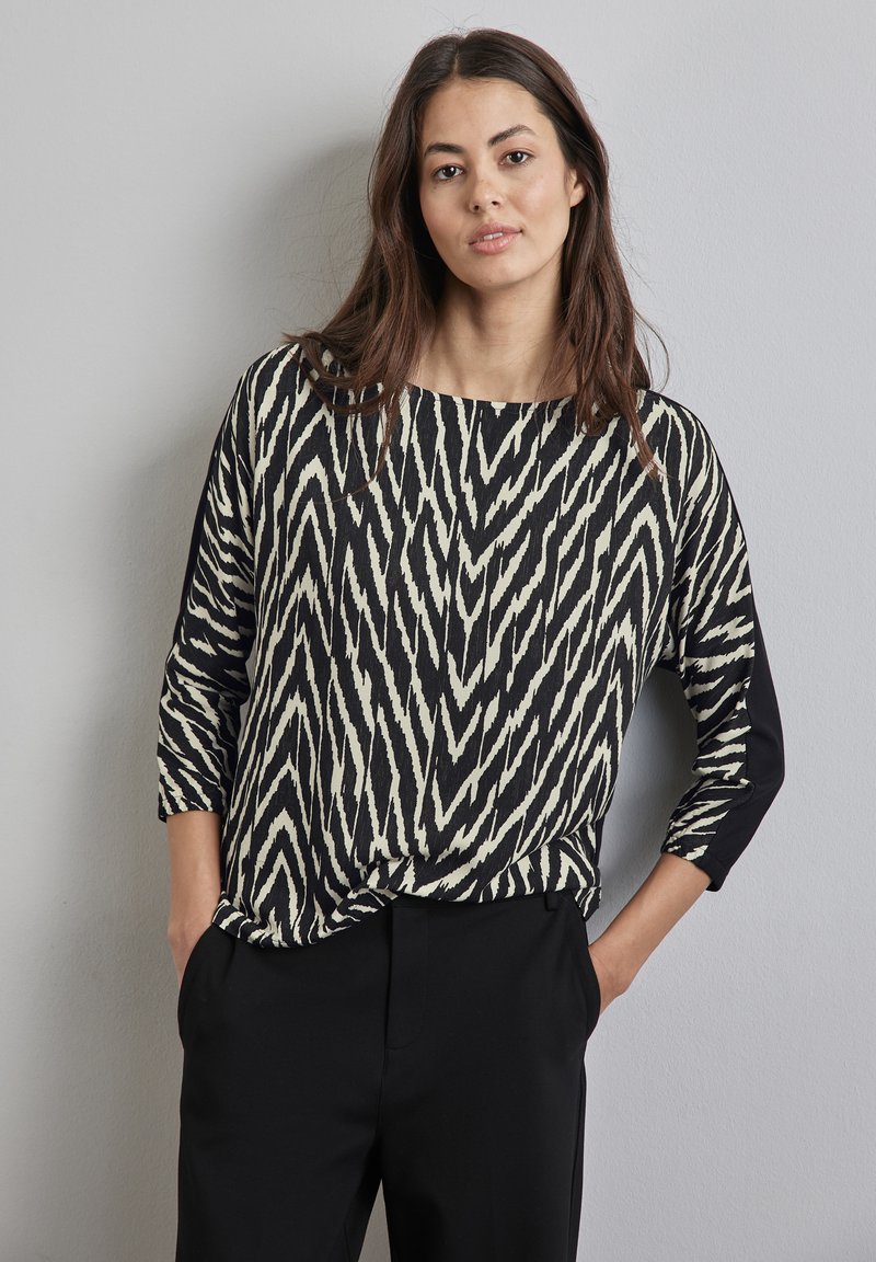 Czarny i kremowy top w wzory z dekoltem łódkowym i rękawami dosięgającymi łokcia; charakteryzuje się kontrastującym czarnym detalem z boku oraz luźnym krojem.