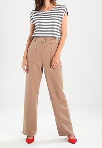 Top de rayas gris y blanco de manga corta combinado con pantalones beige de cintura alta que cuentan con un cinturón. La modelo lleva unos tacones rojos de punta.