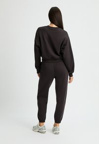 Sudadera negra y pantalones ajustados a juego en tejido suave. Puños y cintura acanalados, con elástico en el tobillo. Zapatillas de running plateadas.