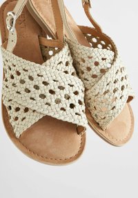 Gewebte beige Sandalen mit Kreuzdesign, Lederakzenten und einer natürlichen Wildledersohle; mit einem verstellbaren Schnallenverschluss für einen sicheren Sitz.