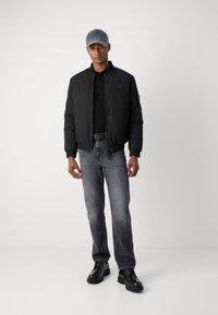 Svart bomberjakke, svart polo-skjorte, grå jeans og svarte snørebåndsko. Grå caps. Glatt stoff, tettsittende design, uformell stil.