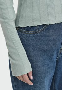 Lichtgroene geribde lange mouw top met een gekartelde zoom, gecombineerd met donkerblauwe denim jeans, voorzien van een klassiek zakontwerp en standaard stiksel.