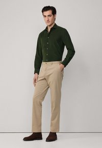 Zielona koszula z długim rękawem, zapinana na guziki, o gładkiej fakturze. Beżowe chinosy o prostym kroju z bocznymi kieszeniami. Ciemnobrązowe botki za kostkę.