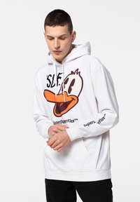 Valge kapuutsiga pusa, millel on suur oranž ja must karikatuurne part. Sisaldab nööre, eesmist taskut ja teksti "SuperDuperFlex™".