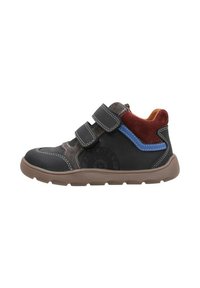 Zapatilla deportiva en negro y marrón con dos correas de Velcro, acentos de ante en rojo y azul, y una suela de goma texturizada. Vista de perfil lateral.