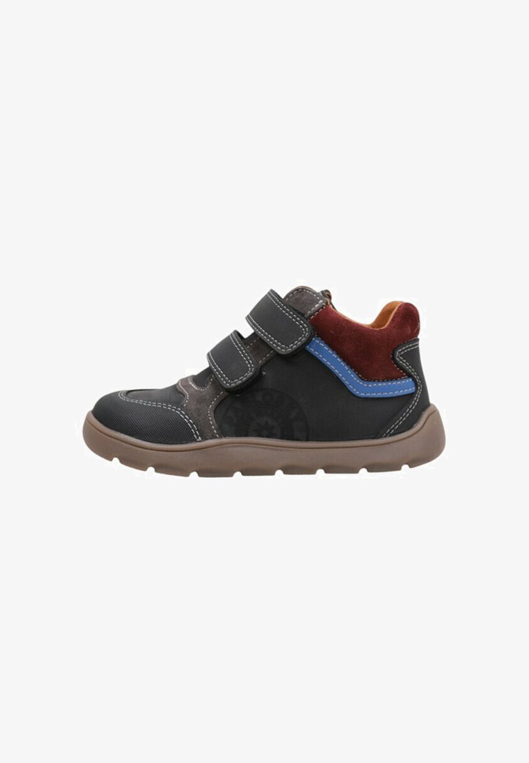 Zapatilla deportiva en negro y marrón con dos correas de Velcro, acentos de ante en rojo y azul, y una suela de goma texturizada. Vista de perfil lateral.