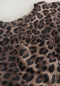 Tkanina majice s uzorkom smeškastih leopardnih mrlja u smeškastoj boji, s okruglim izrezom i džepom na prsima. Odlikuje se glatkom teksturom i kontrastnim crnim mrljama.