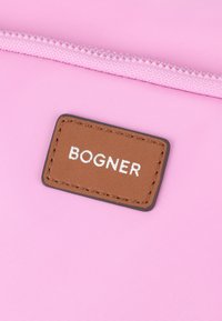 Rosa tygväska med en brun läderetikett där "BOGNER" är präglat och en silverkant runtom. Texturerad dragkedjedetalj högst upp.