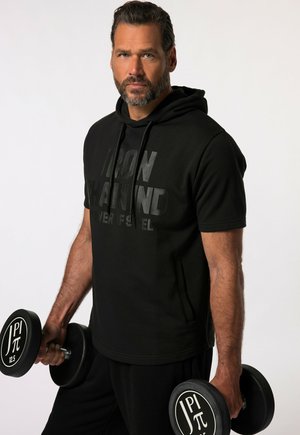 Zwarte hoodie met korte mouwen en een matte "IRON" opdruk. Het model houdt een zwarte dumbbell vast met een ronde gewichtlabel en draagt bijpassende zwarte broek.