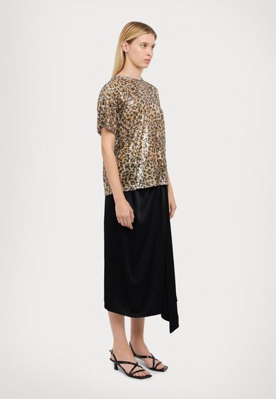 Top in paillettes leopardato oro e nero con maniche corte, abbinato a una gonna nera con un design drappeggiato. Ambientato su uno sfondo neutro.