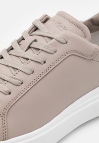 Baskets en cuir beige clair avec lacets plats, surpiqûres ton sur ton et semelle en caoutchouc blanche. Présentent un logo discret embossé sur la languette.