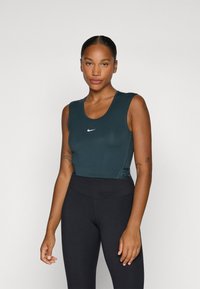Top sportiv teal, cu decolteu rotund, având un logo Nike alb și o bandă texturată. Asortat cu leggings negri cu talie înaltă.