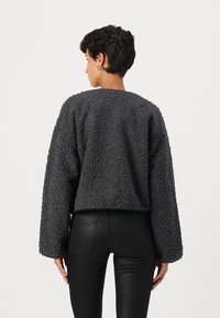 Pull en gris à texture floue, avec des épaules drop et une coupe courte, associé à un pantalon noir ajusté.