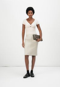 Beige bodycon top s twist detailem, spárovaný se smetanovou tužkovou sukní. Černé lesklé boty a strukturovaná tmavozelená kabelka.