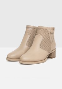 Bottines beige avec une finition en cuir lisse et des accents perforés, dotées d'un talon empilé et de panneaux latéraux élastiques pour un enfilage facile.