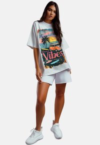 White oversized t-shirt with a colorful graphic of a van and palm trees, paired with white shorts and white sneakers.