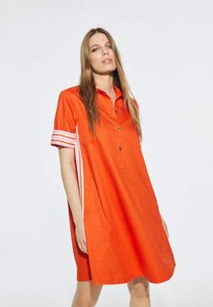 Robe orange courte avec un col boutonné, présentant des rayures blanches sur les manches et des poches latérales. Tissu lisse avec une coupe décontractée.