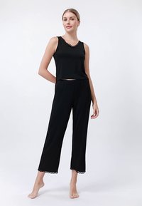 Melns atpūtas tērpa komplekts ar bezroku topu, kas rotāts ar mežģīņu apdari, un brīva piegriezuma biksēm ar atbilstošu mežģīņu akcentu apakšmalā.