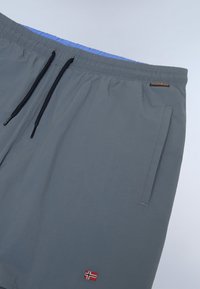 Grey swim shorts with an elastic waistband, blue inner lining, drawstring, two side pockets, and a small embroidered flag detail.