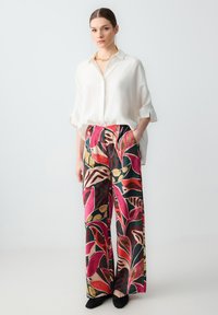 Camicia button-up bianca in lino e pantaloni a gamba larga con un vivace motivo floreale multicolore. Completano l'outfit delle ballerine nere.
