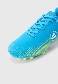 Μπλε ποδοσφαιρικό παπούτσι με κίτρινες λεπτομέρειες, δεμένα κορδόνια και καλουπωμένες τάπες, απομονωμένο σε λευκό φόντο.