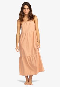 Maxime dress in light peach fabric, featuring a tiered design, adjustable spaghetti straps, and a relaxed fit. Smooth texture with a flowing silhouette.