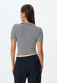 Kortärmad, kort topp med svart och vita horisontella ränder, ribbad struktur och krage. Matchas med mörka, skräddarsydda byxor.