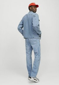 Chaqueta de mezclilla azul claro y jeans a juego, con un corte relajado. Gorro rojo y zapatillas multicolor completan el atuendo.