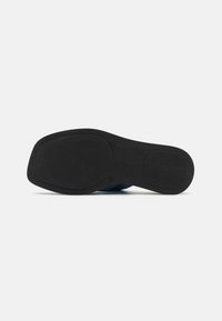Sole nera con una superficie liscia e texture; presenta una forma arrotondata e una curvatura minima. Il materiale appare resistente e flessibile.