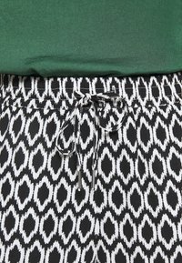 Pantalon à motif géométrique noir et blanc avec taille à cordon noué, associé à un top en tissu vert.