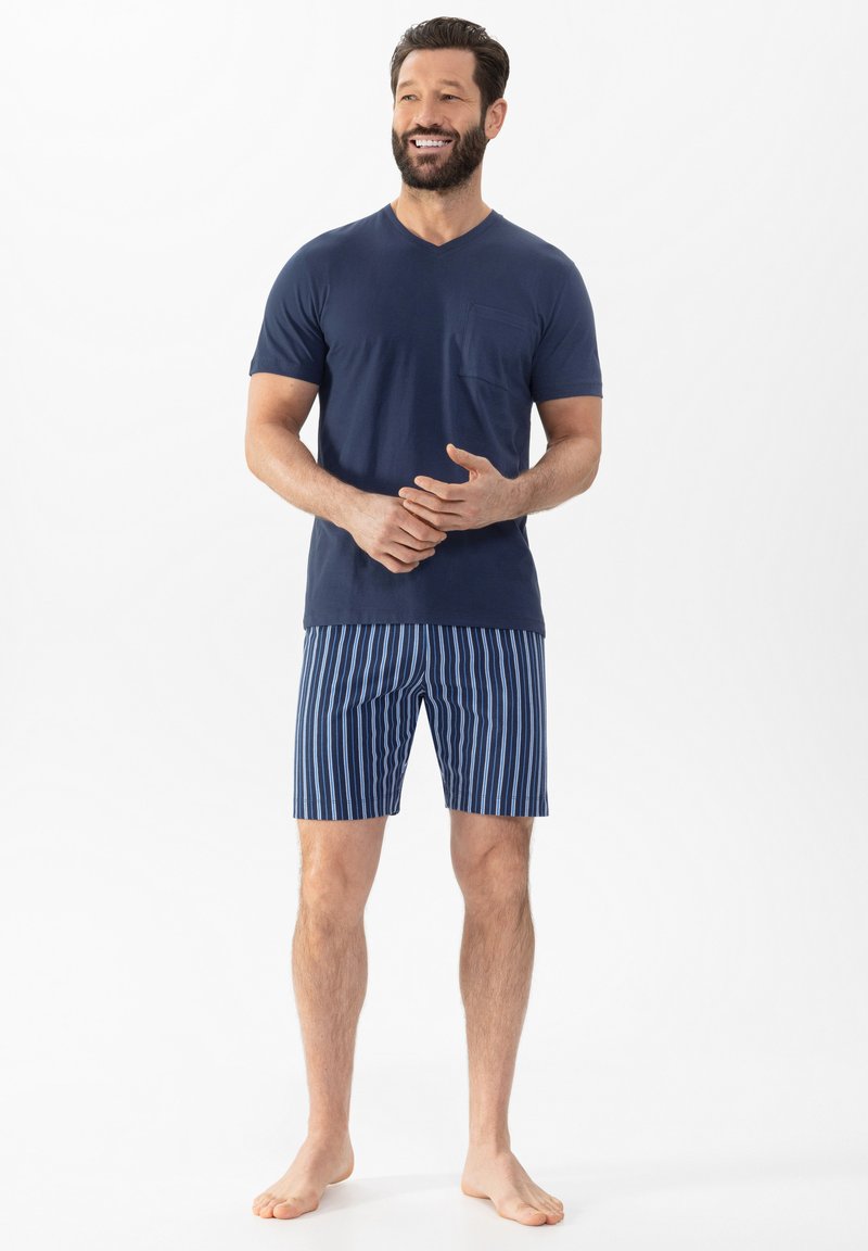 T-shirt bleu marine à col en V avec une poche sur la poitrine, associé à un short rayé bleu marine et blanc. Le tissu semble doux ; le short a une taille élastique.