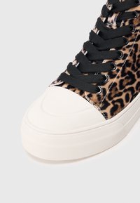 Tenisi din pânză cu imprimeu leopard, cu șireturi negre, vârful din cauciuc alb și talpă texturată. Accent pe designul stilat și detaliile vibrante ale modelului.