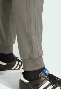 Gray athletic pants with three side stripes, elastic cuffs, paired with black sneakers featuring white stripes and blue accents.