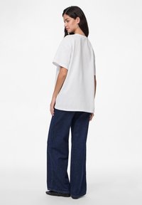 Hvit oversized t-skjorte med rund hals, kombinert med løse mørkeblå denimbukser og svarte flate sko. Enkel tekstur, uten mønstre.